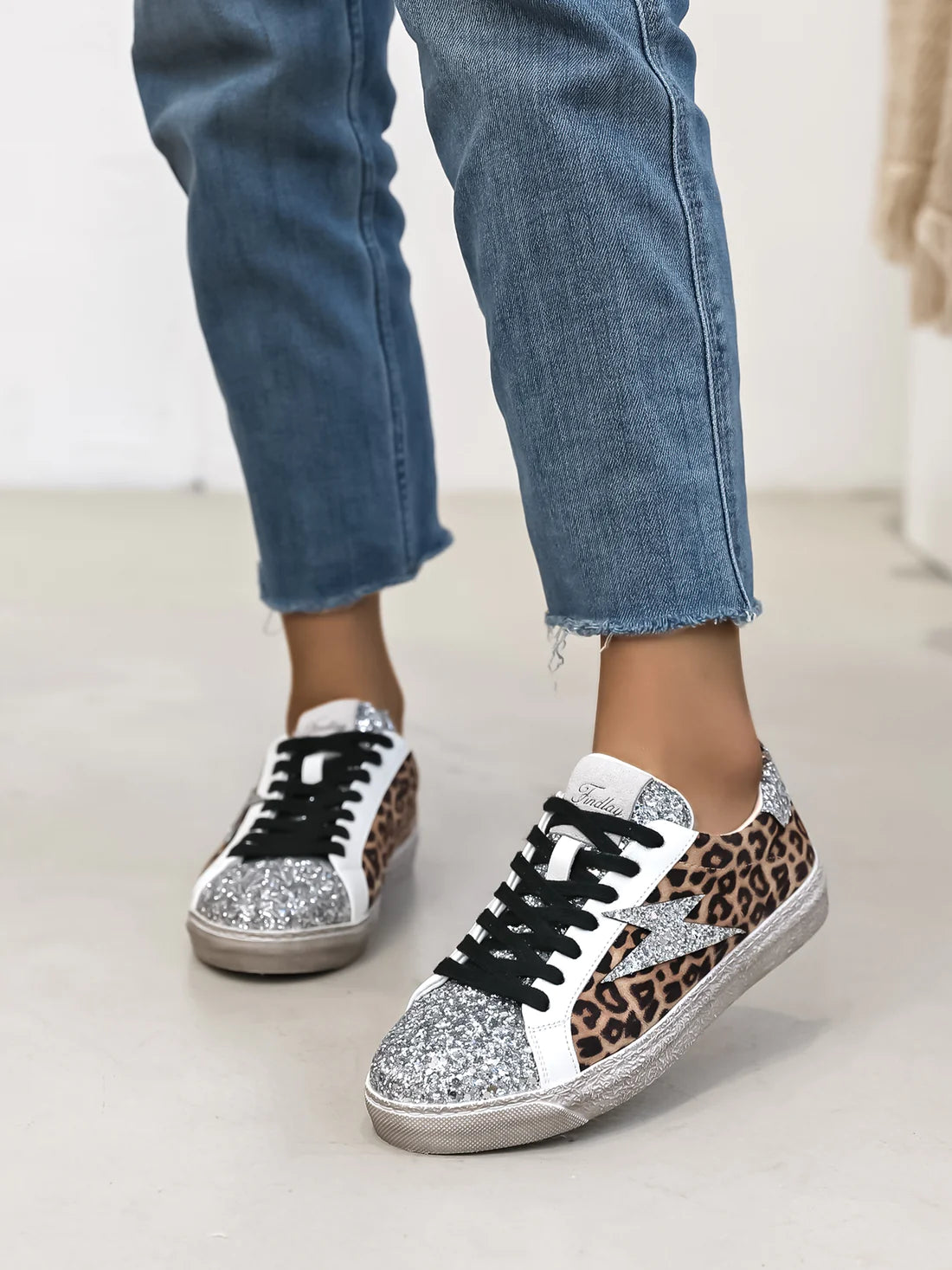 Notre basket Romy en suédine léopard et paillettes argentées est l'accessoire parfait pour un look unique et original. Avec sa découpe en éclair sur les côtés, elle apporte une touche de fantaisie à toutes vos tenues. Confortable et tendance, elle ne pourra que vous séduire !